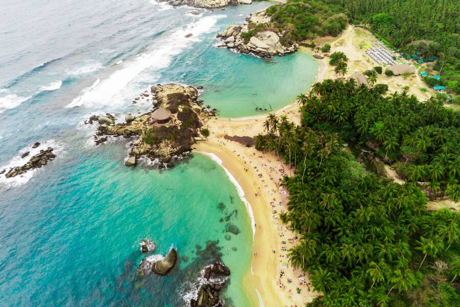 Une rivière coule sur des formations rocheuses parsemées de cavités circulaires, où des plantes aquatiques rouges colorent l'eau transparente, créant de petites cascades à effet de filé.