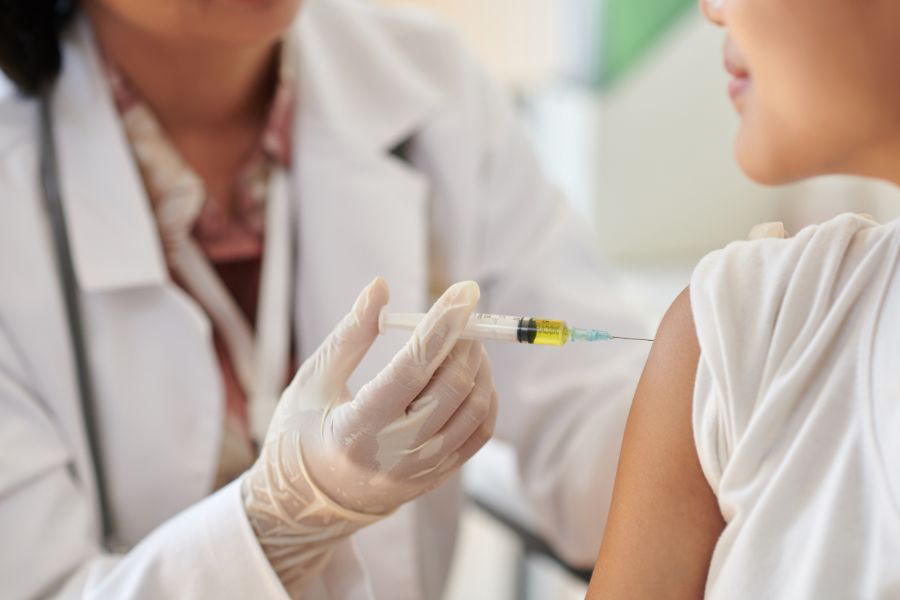 Un professionnel de santé prépare une seringue de vaccin à côté d’un passeport posé sur une table médicale lumineuse.