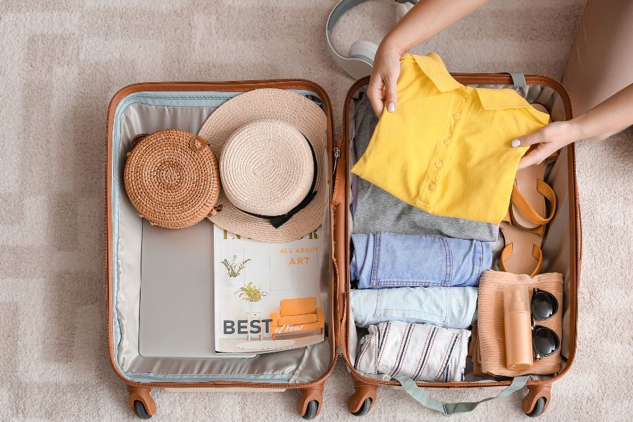 Des vêtements pliés, un appareil photo et des accessoires de voyage sont soigneusement rangés à l’intérieur d’une valise ouverte posée sur le sol.