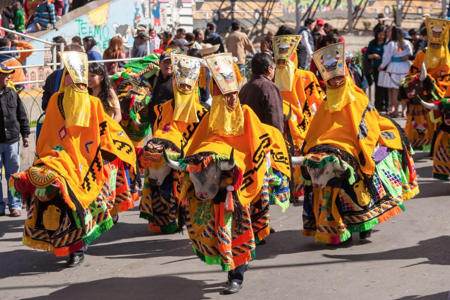 Des danseurs en costumes traditionnels jaunes ornés de têtes de taureau défilent dans une rue bordée de spectateurs lors d'une fête populaire.