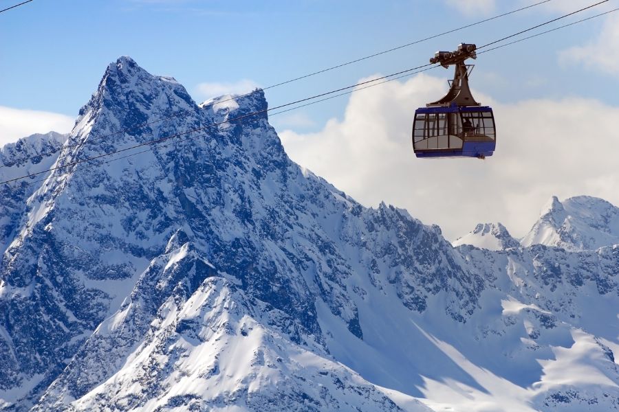 Une cabine de téléphérique bleue glisse le long d'un câble devant de hauts sommets alpins recouverts de neige.