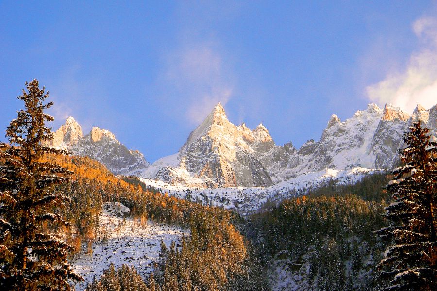 Des aiguilles rocheuses enneigées s'élèvent au-dessus d'une forêt de conifères baignée par la lumière du soleil couchant.