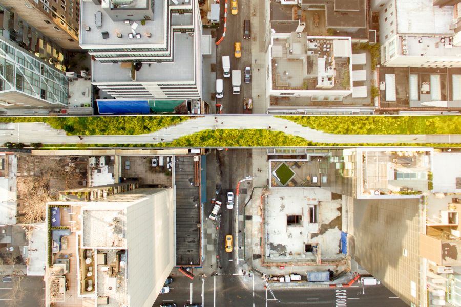 Une vue aérienne plongeante montre un parc suspendu verdoyant traversant un quartier urbain au-dessus de rues animées par le trafic automobile.