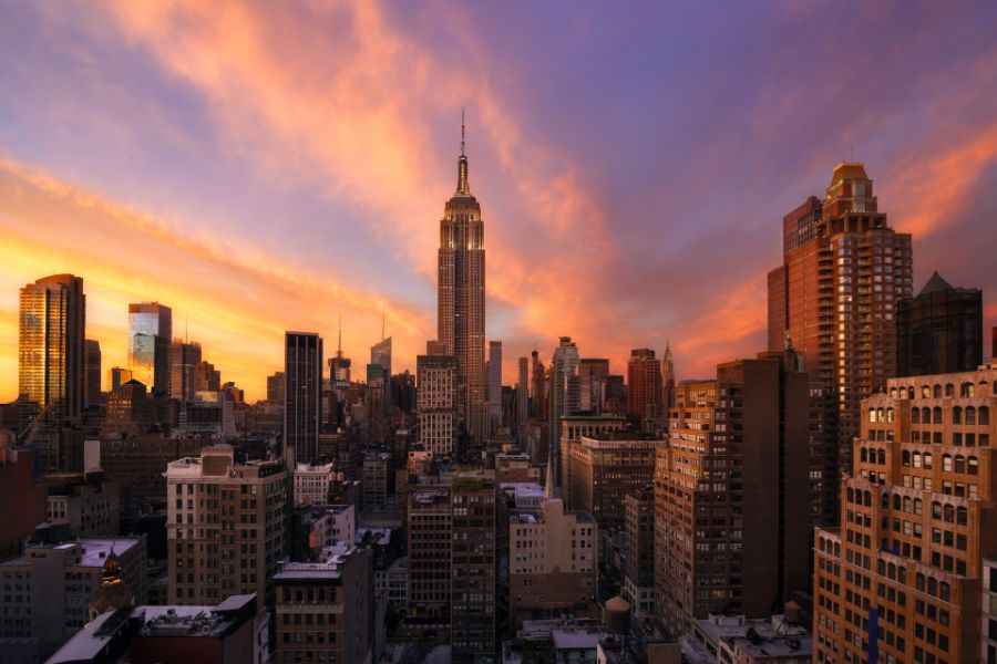 Les gratte-ciels illuminés du centre-ville de Manhattan s'élèvent sous un ciel crépusculaire aux nuances orange et bleues.