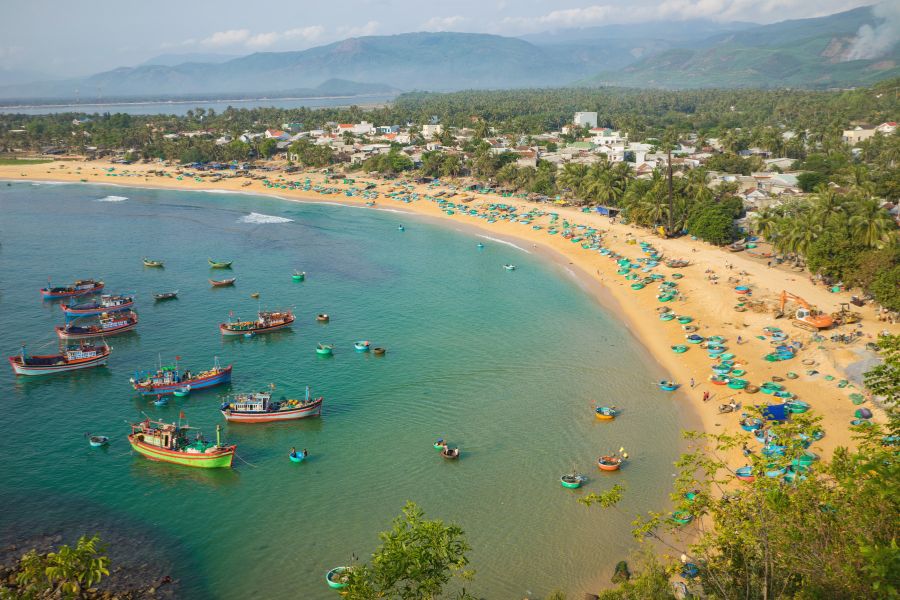 Une large baie circulaire aux eaux bleu azur est entourée de collines arides et de plages de sable sous un ciel dégagé.