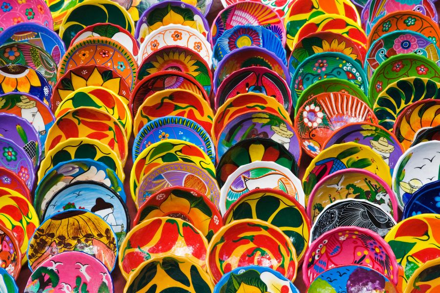 Une multitude de bols en céramique artisanale peints à la main aux motifs floraux et géométriques multicolores sont alignés et superposés sur un étal de marché.