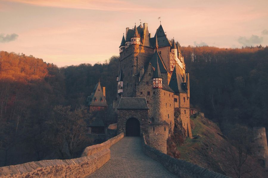 Un château médiéval en pierre aux tourelles pointues se dresse au cœur d'une forêt aux couleurs automnales.