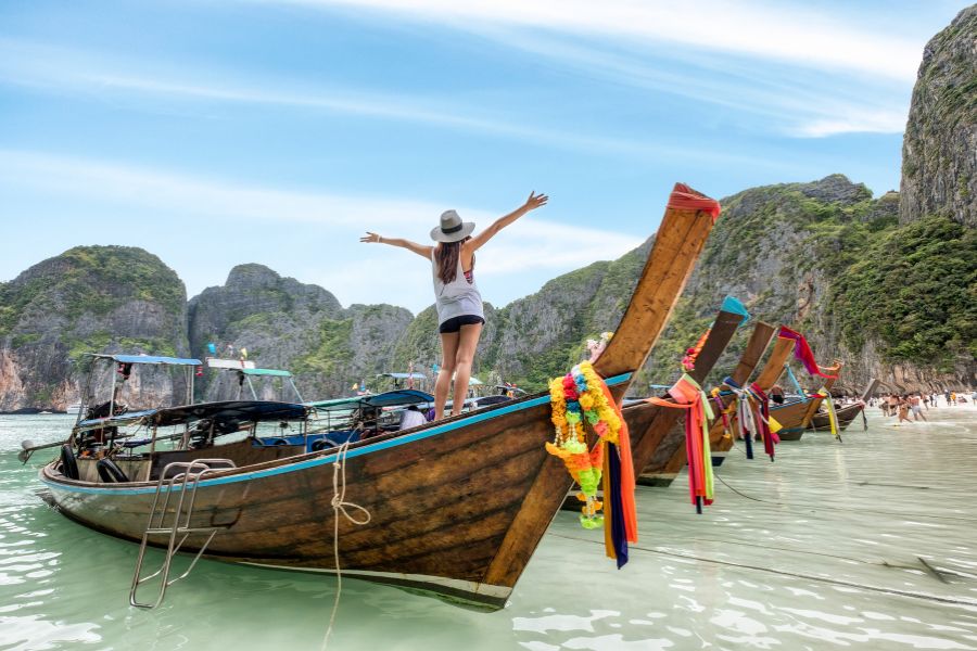 Une baie tropicale avec des bateaux traditionnels en bois amarres près de rochers recouverts de végétation verdoyante sous un ciel nuageux.