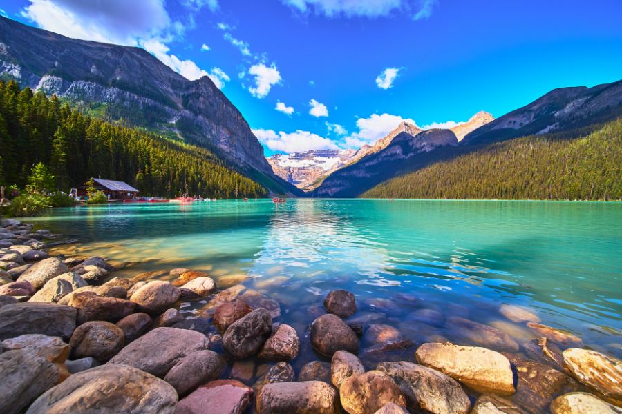 Un lac aux eaux turquoise s'étend au pied de montagnes rocheuses escarpées et enneigées, bordé d'une forêt de conifères.