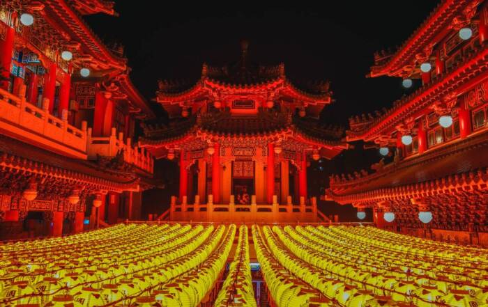 Un majestueux temple chinois aux couleurs rouge et blanche illuminé pendant la nuit, avec des lanternes traditionnelles suspendues, une architecture asiatique richement décorée, des détails dorés raffinés et une atmosphère paisible sous un ciel nocturne sombre.