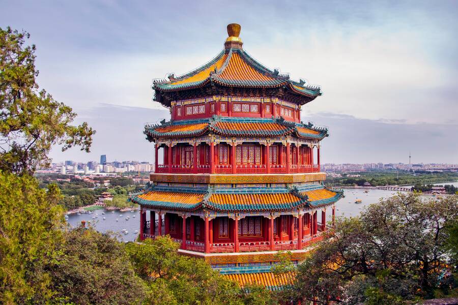 Pavillon traditionnel chinois richement décoré dominant un paysage naturel et urbain, entouré d’arbres verdoyants avec vue panoramique sur un lac paisible et la ville à l’horizon sous un ciel lumineux.