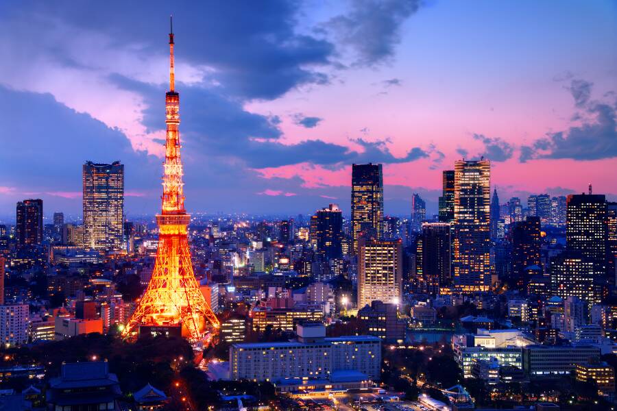 La Tokyo Tower illuminée en orange vif domine un immense paysage urbain de gratte-ciels scintillants sous un ciel de crépuscule aux nuances violettes et roses.
