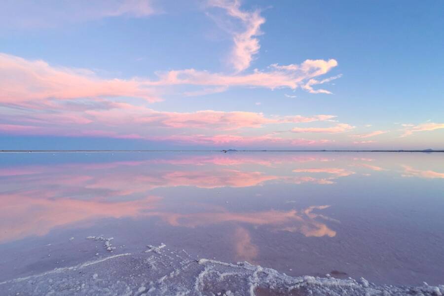 Un ciel aux nuages teintés de rose et de bleu se reflète parfaitement sur l'immense étendue d'eau calme du Salar d'Uyuni, invitant à voyager en Bolivie.