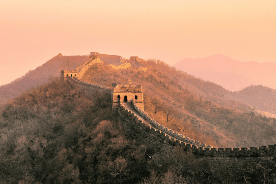La Grande Muraille de Chine serpente le long de crêtes montagneuses baignées par la lumière dorée d'un coucher de soleil.