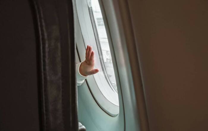 Petite main d'enfant sur un hublot d'avion en plein vol avec vue sur le ciel bleu et les nuages.