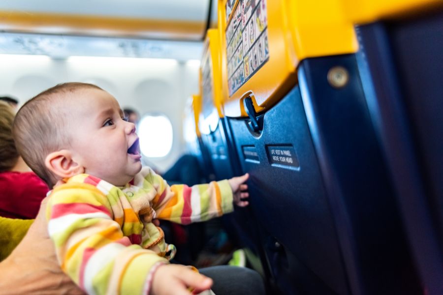Un bébé en tenue rayée regarde joyeusement vers le haut et touche le dossier jaune du siège devant lui dans la cabine d'un avion.