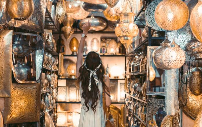 Une femme vue de dos pointe du doigt une lanterne parmi une multitude de lampes artisanales en métal sculpté et illuminées dans une boutique d'artisanat.