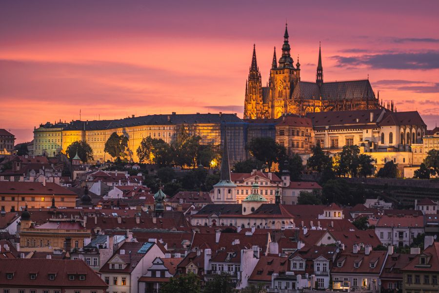 Le château médiéval et la cathédrale s'élèvent au-dessus d'un panorama de toits en tuiles sous un ciel crépusculaire aux nuances rose et orange.
