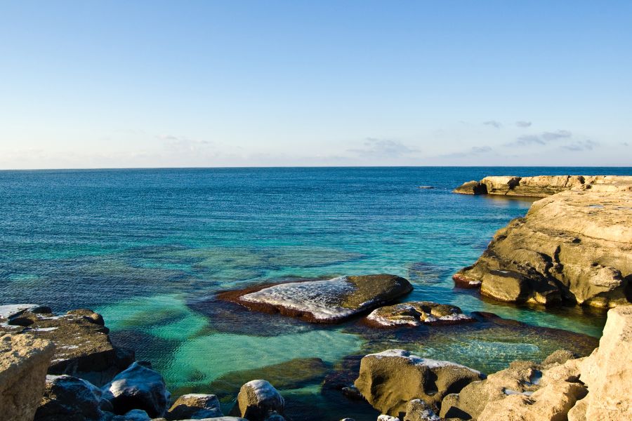 Des formations rocheuses bordent une eau claire et turquoise s'étendant jusqu'à l'horizon sous un ciel dégagé.