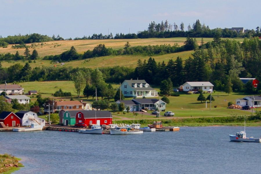 De petites maisons de pêcheurs colorées bordent un port où mouillent quelques bateaux au pied de collines verdoyantes.