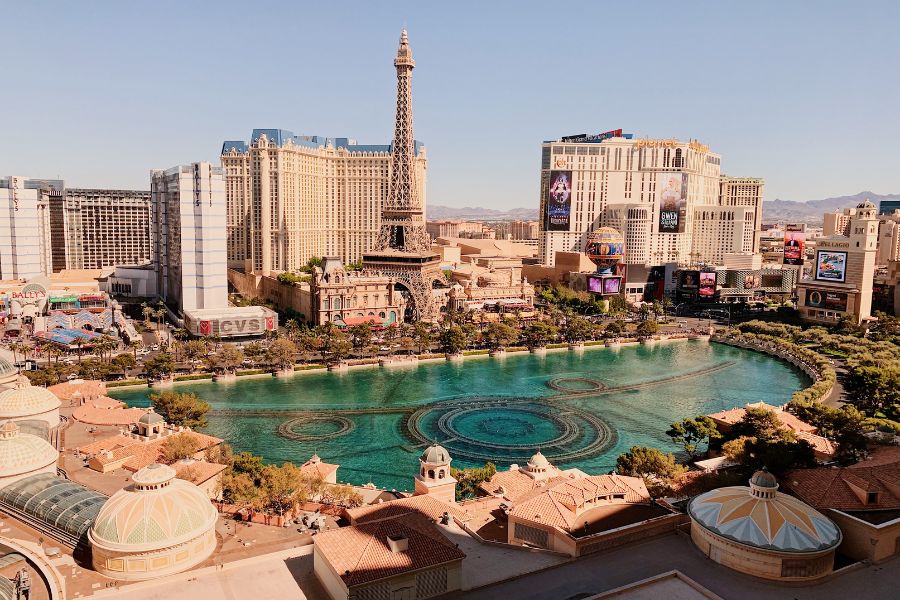 Un vaste bassin d'eau s'étend au premier plan devant des hôtels imposants et une réplique de la tour Eiffel sous un grand ciel bleu.